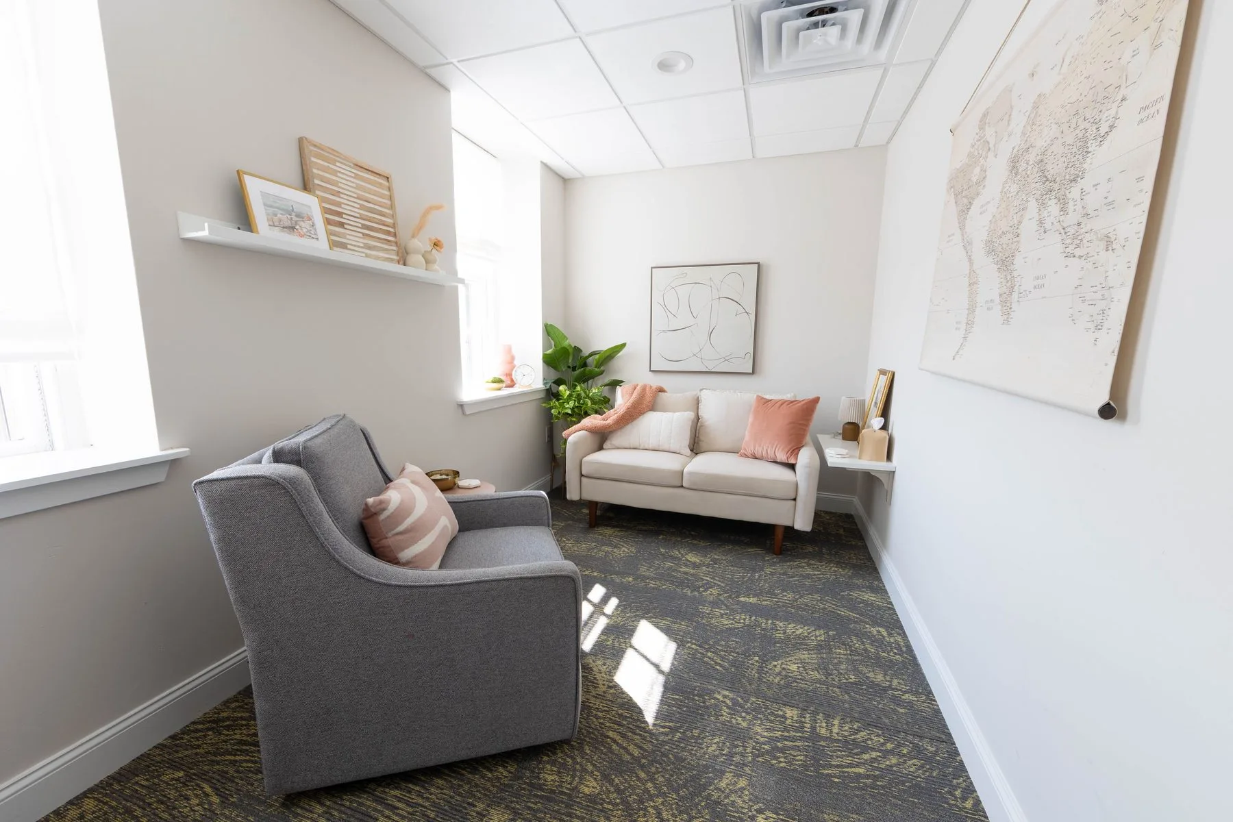 Therapy room at Brave Embers Wellness, Doylestown — a gray armchair facing a cream sofa with blush pillows beneath sunlit windows.