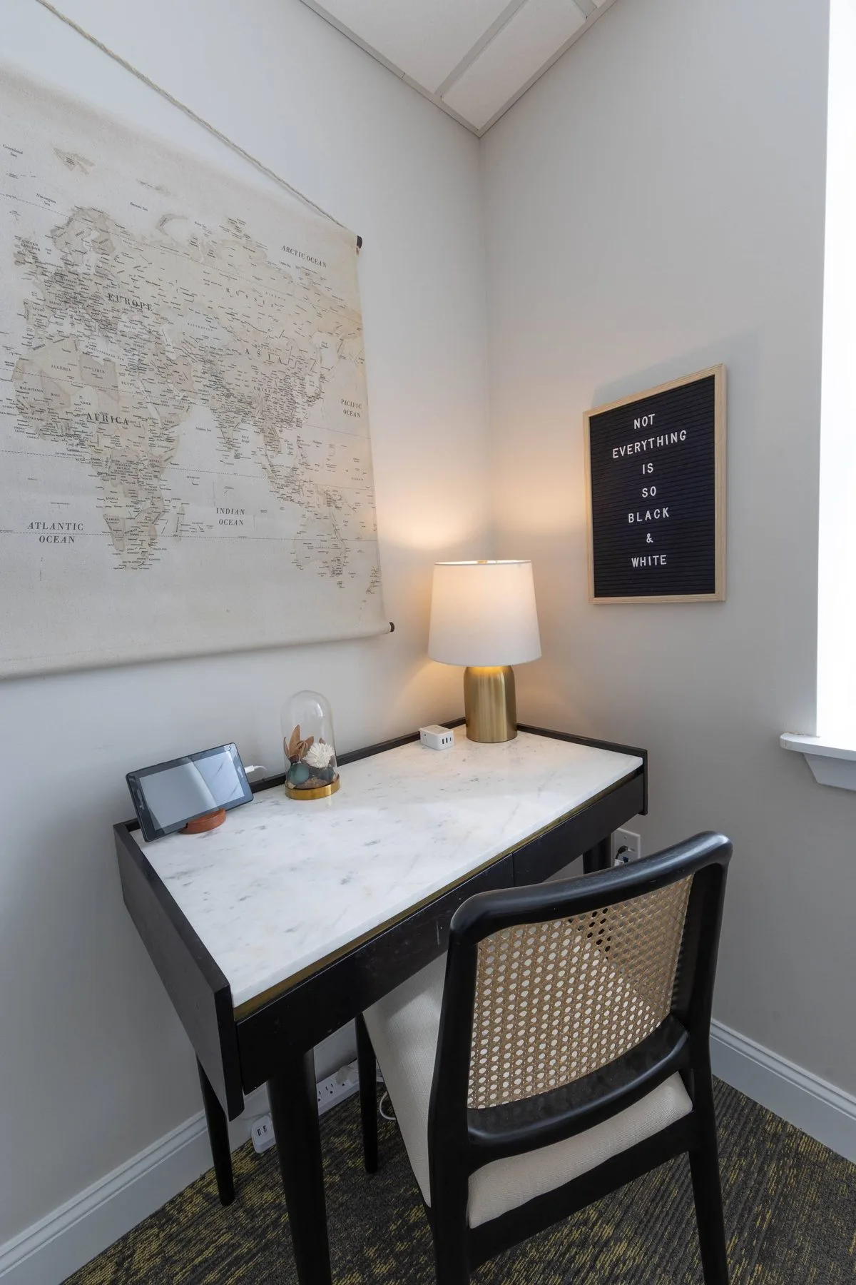 Quiet desk nook with a lamp, a canvas world map and a letterboard reading “Not everything is so black & white.”