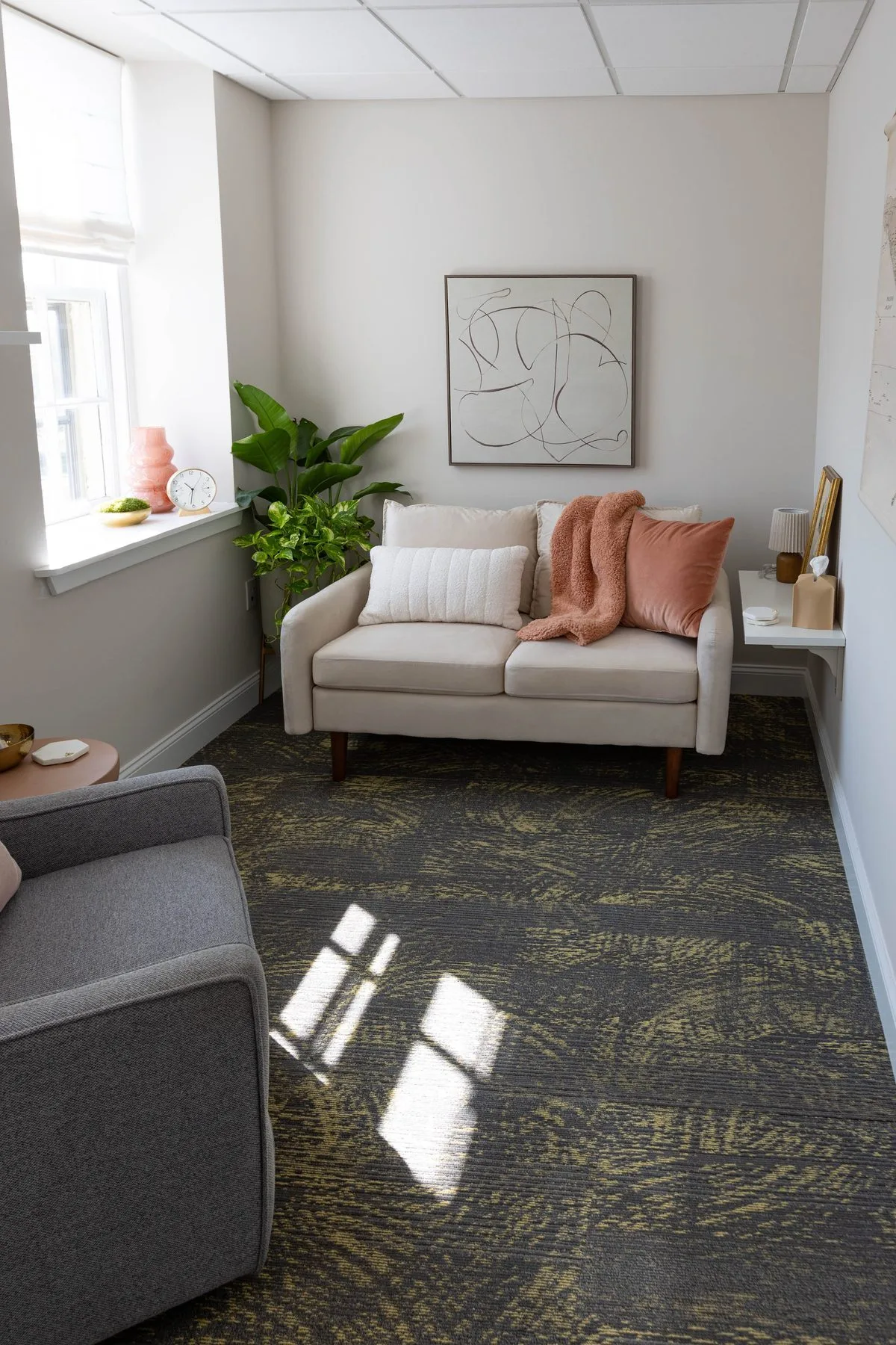 Cream sofa with a rust throw and a trailing plant beside a window, with afternoon light falling across the carpet.